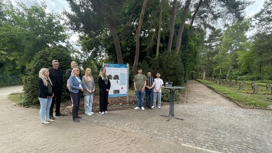 Schülergruppe rechts und links von der Informationstafel. Außerdem Schulleiter und Bürgermeisterin links neben der Tafel stehend. 